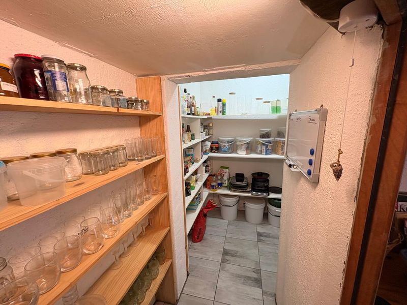 A functional walk-in pantry or scullery area featuring extensive built-in timber shelving and durable tiled flooring for organized storage.