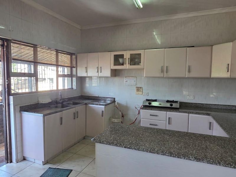 A functional kitchen featuring granite countertops, ample built-in cabinetry, a gas hob, and tiled finishes, offering a practical layout for daily use.