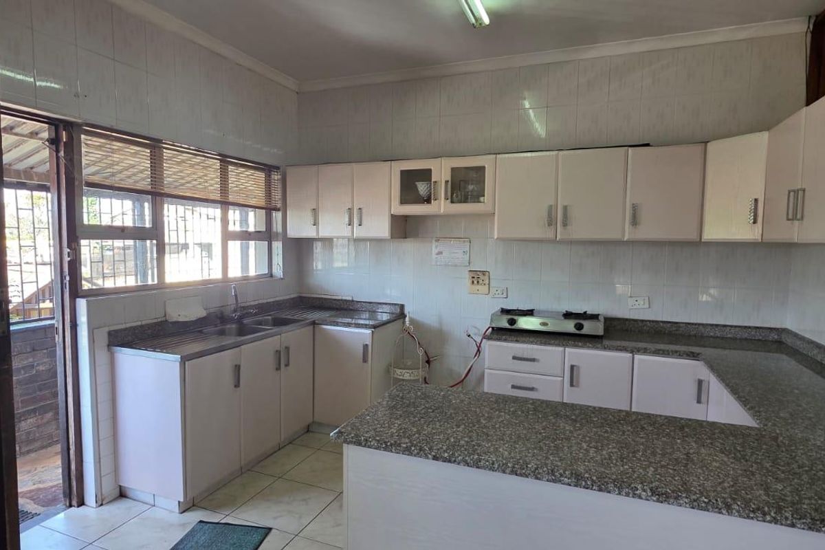 A functional kitchen featuring granite countertops, ample built-in cabinetry, a gas hob, and tiled finishes, offering a practical layout for daily use.