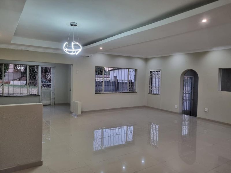 Spacious, open-plan living area featuring polished porcelain floor tiles, recessed ceiling detail, and secure window bars.