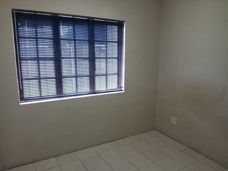 A clean, empty bedroom featuring neutral tiled flooring, a window with fitted blinds, and a standard electrical outlet.