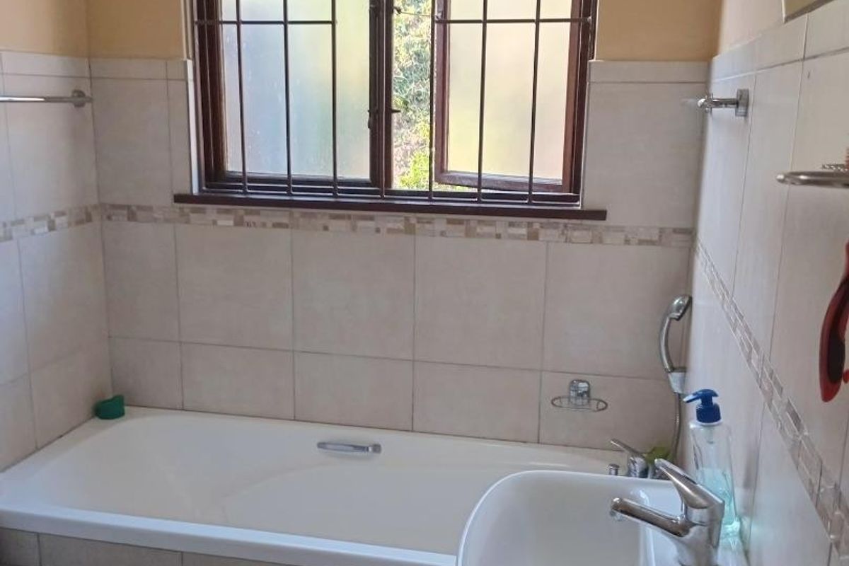 A functional bathroom featuring a bathtub, pedestal basin, and neutral wall tiling with decorative border accents.