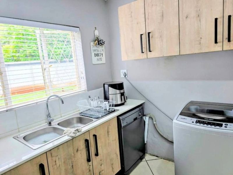 Functional laundry area featuring a double stainless steel sink, laminate cabinetry, and tiled flooring with convenient plumbing connections for appliances.
