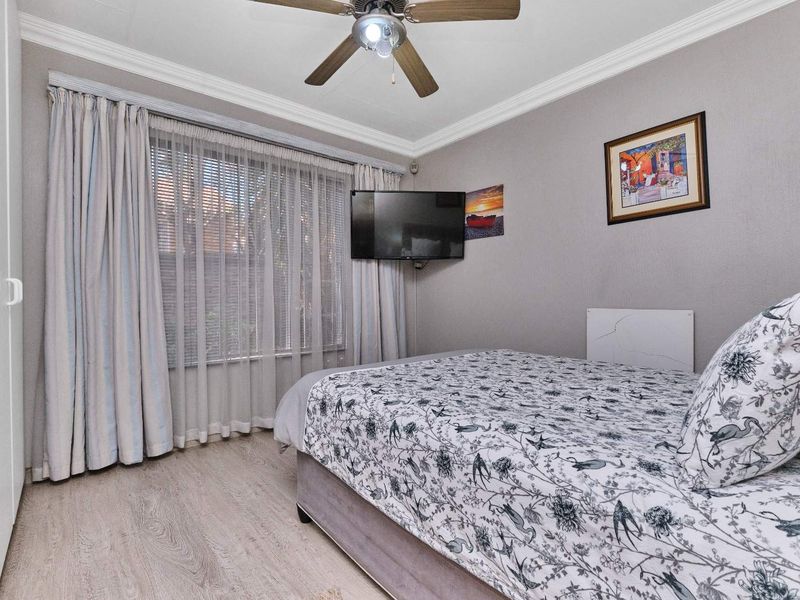 A well-maintained bedroom featuring laminate flooring, crown molding, a ceiling fan, and built-in wardrobe storage.