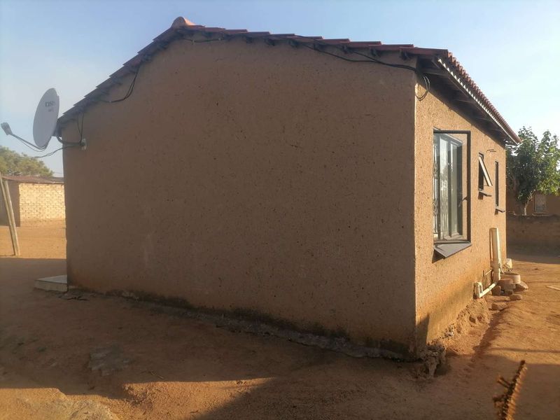 Rear view of a single-story dwelling featuring a tiled roof, casement window, and visible exterior wall maintenance requirements.