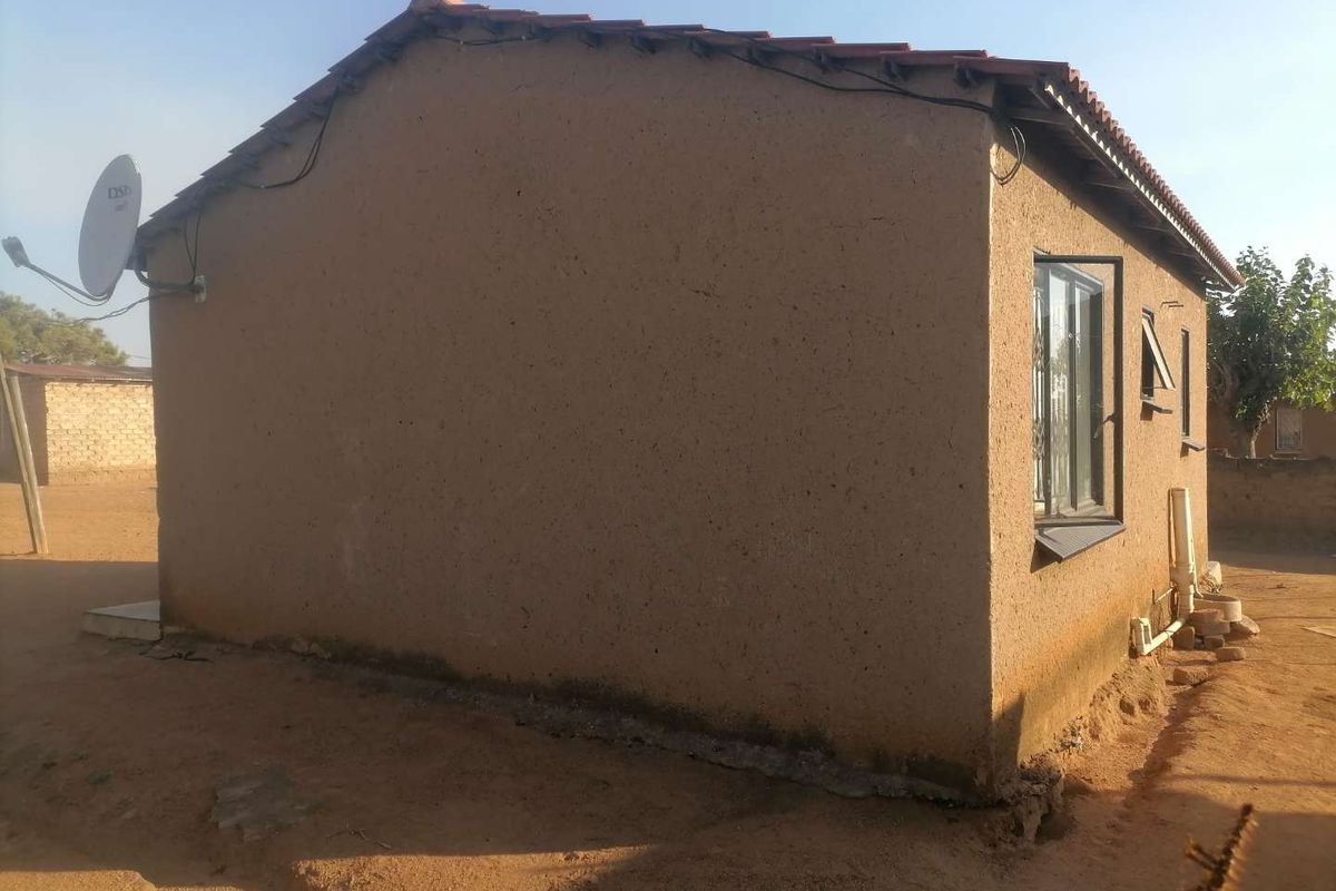 Rear view of a single-story dwelling featuring a tiled roof, casement window, and visible exterior wall maintenance requirements.