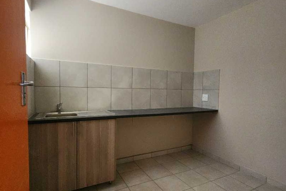 A compact, empty kitchen area featuring tiled flooring, a neutral backsplash, and basic base cabinetry with a sink and countertop.