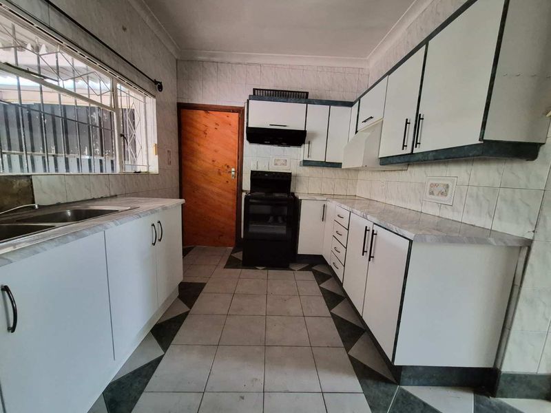 A functional kitchen featuring white cabinetry, laminate countertops, tiled flooring, and a built-in extractor fan, offering a clean space ready for updates.