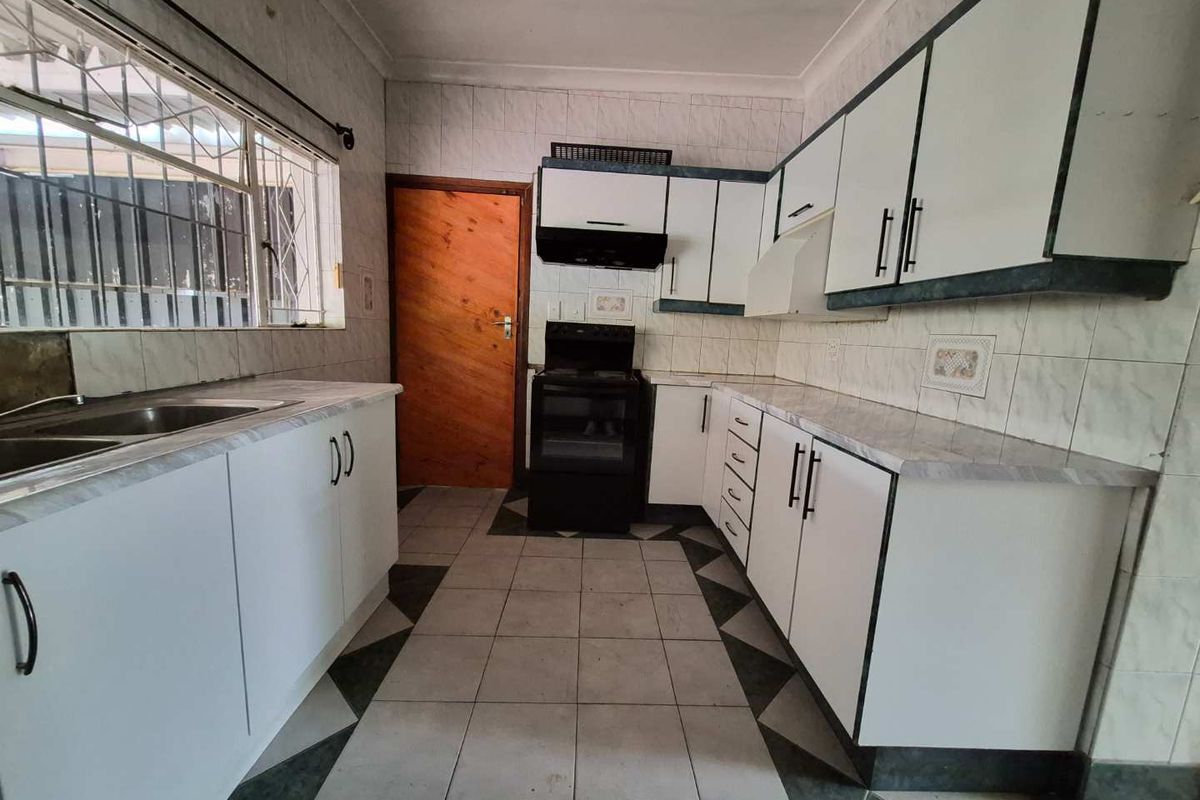 A functional kitchen featuring white cabinetry, laminate countertops, tiled flooring, and a built-in extractor fan, offering a clean space ready for updates.