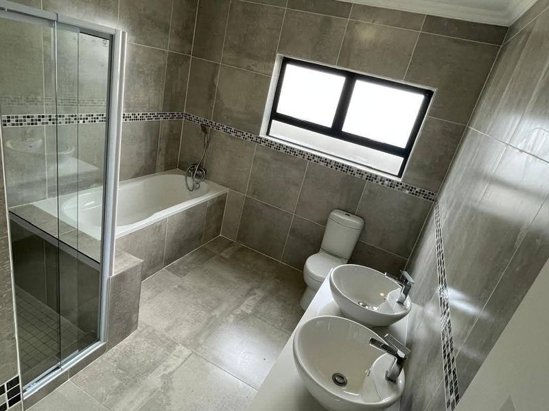 Modern bathroom featuring a built-in bathtub, glass-enclosed shower, dual vessel sinks with chrome fixtures, and contemporary grey floor-to-ceiling tiling.