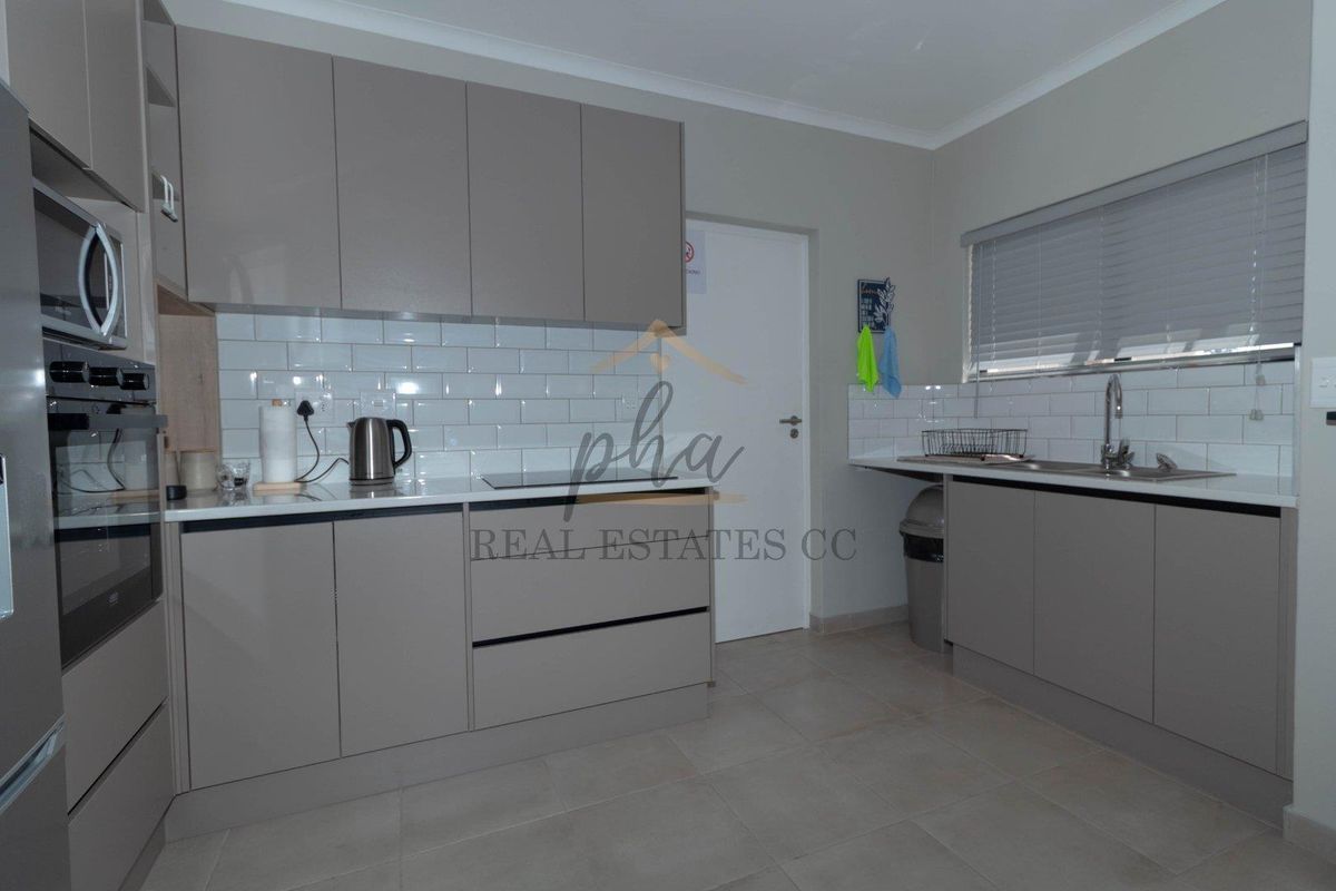 Modern kitchen featuring sleek grey cabinetry, white subway tile backsplash, integrated oven, and a stainless steel sink with a window view.