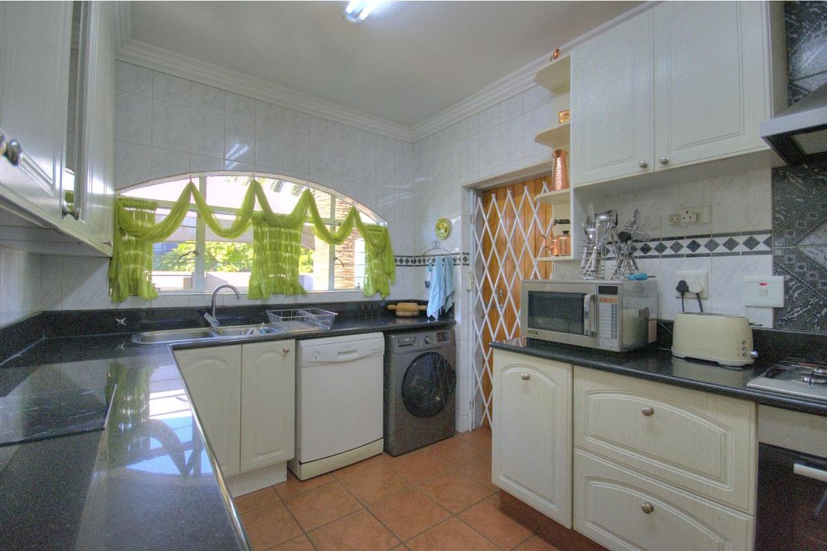 A functional kitchen featuring white cabinetry, dark granite countertops, tiled splashbacks, and integrated space for laundry appliances.