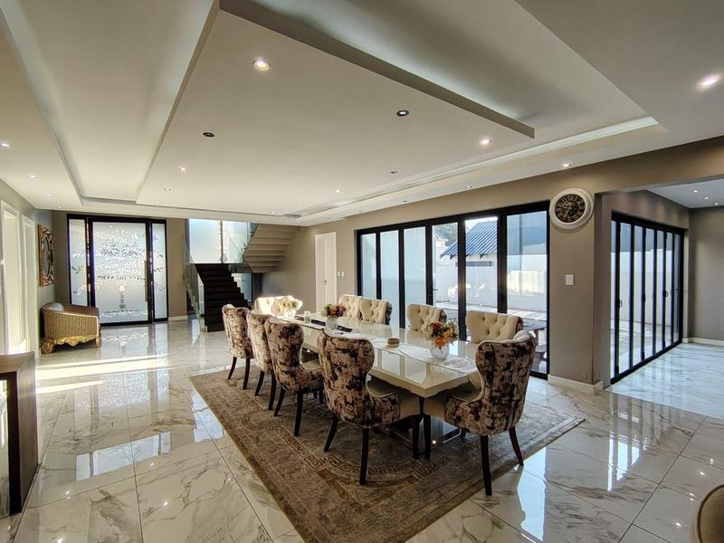 Spacious dining area featuring high-end marble-look flooring, recessed ceiling with integrated lighting, and large black aluminium stacker doors opening to the exterior.