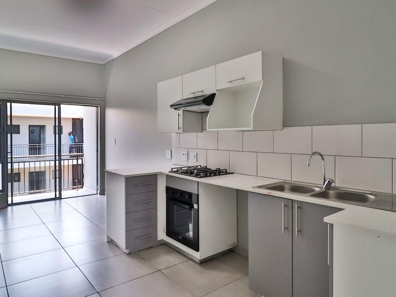 Modern open-plan kitchen featuring built-in cabinetry, gas hob, oven, and tiled finishes, leading directly to a private balcony through sliding glass doors.
