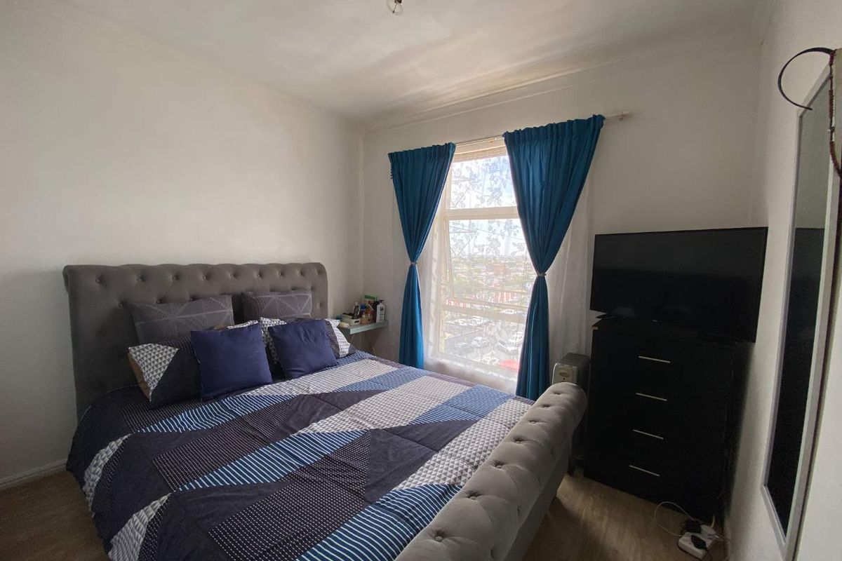 A standard bedroom featuring laminate flooring, a large window with blue curtains, and neutral wall finishes.