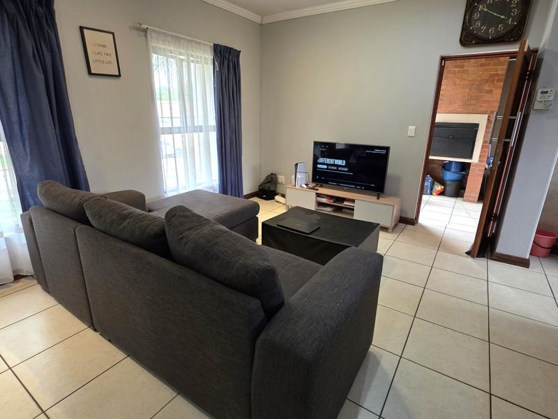 A living room featuring tiled flooring and a view into an adjacent area with a built-in fireplace.