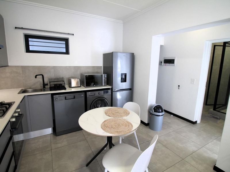 Modern kitchen featuring grey cabinetry, tiled backsplash, gas hob, built-in oven, and integrated plumbing for appliances, with an adjacent dining area.