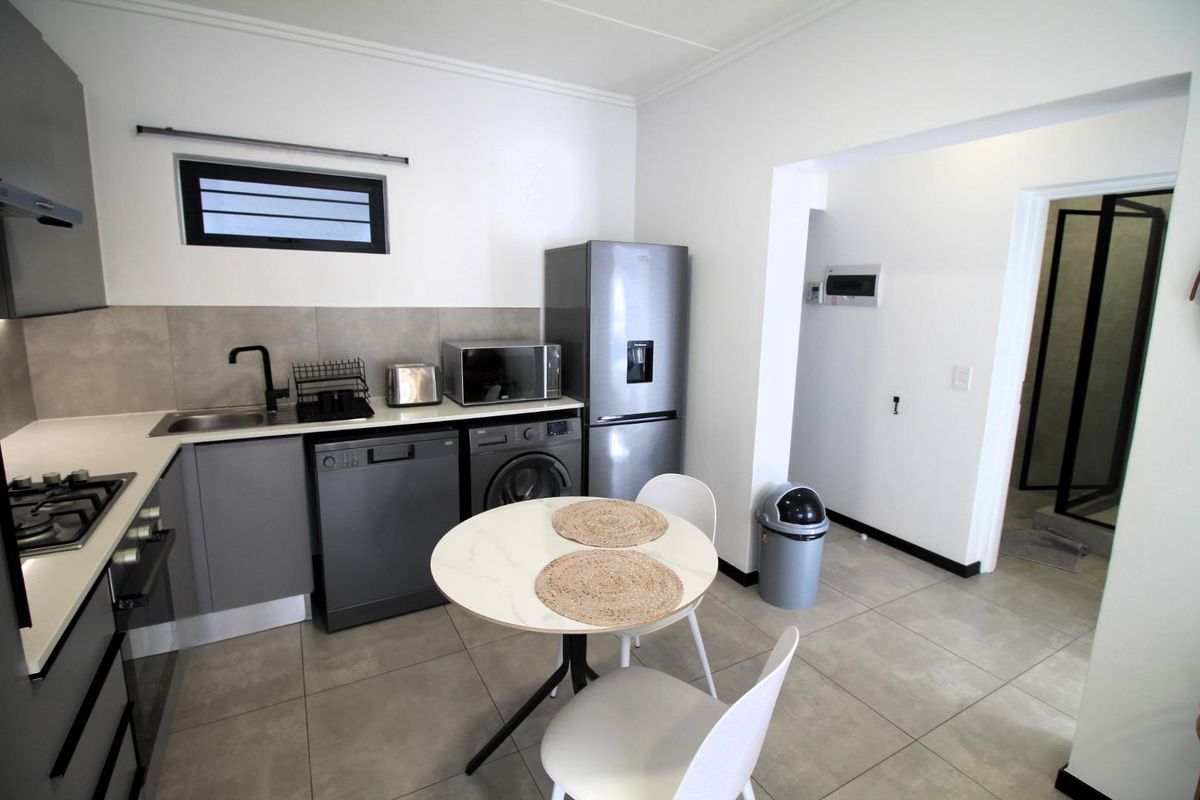Modern kitchen featuring grey cabinetry, tiled backsplash, gas hob, built-in oven, and integrated plumbing for appliances, with an adjacent dining area.