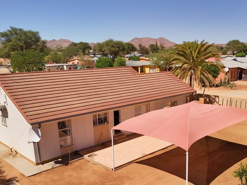 Aerial view of a residential property featuring a tiled roof, a covered patio area with a shade sail, and surrounding boundary walls.