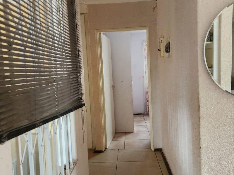 A functional hallway featuring tiled flooring, security gate, and venetian blinds, providing access to adjacent rooms.