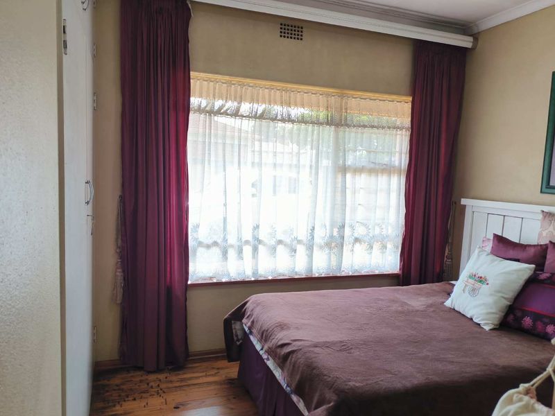 A bedroom featuring timber flooring, built-in cupboards, and a large window with natural light.