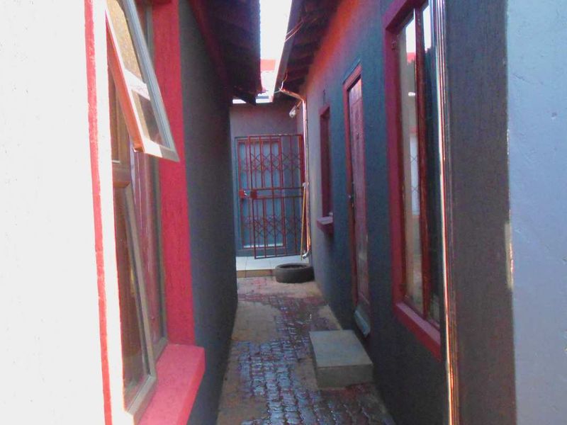 A narrow exterior side passage featuring paved flooring, security gates, and casement windows along the building exterior.