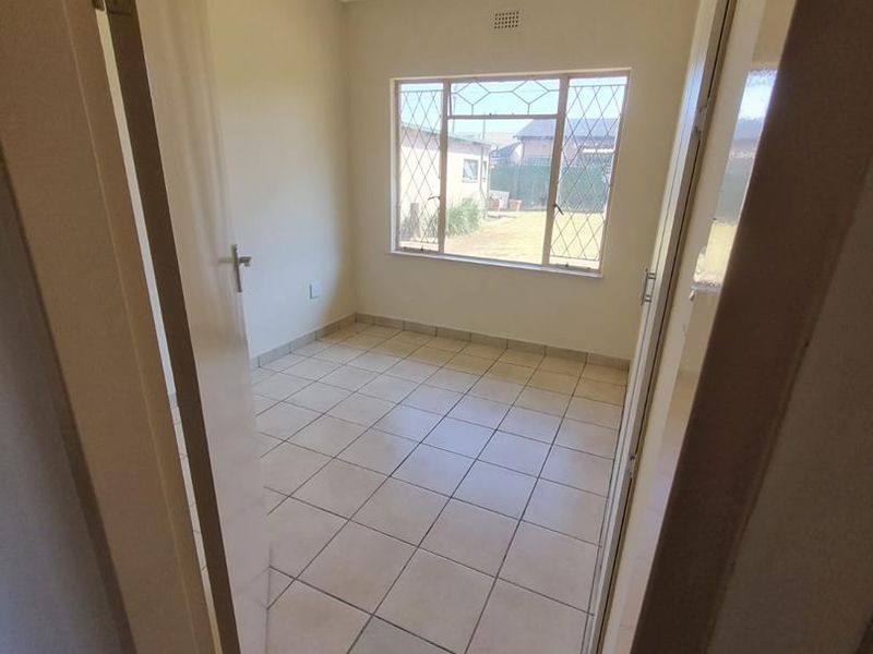 A vacant bedroom featuring neutral tiled flooring, a steel-framed window, and built-in cupboard storage.