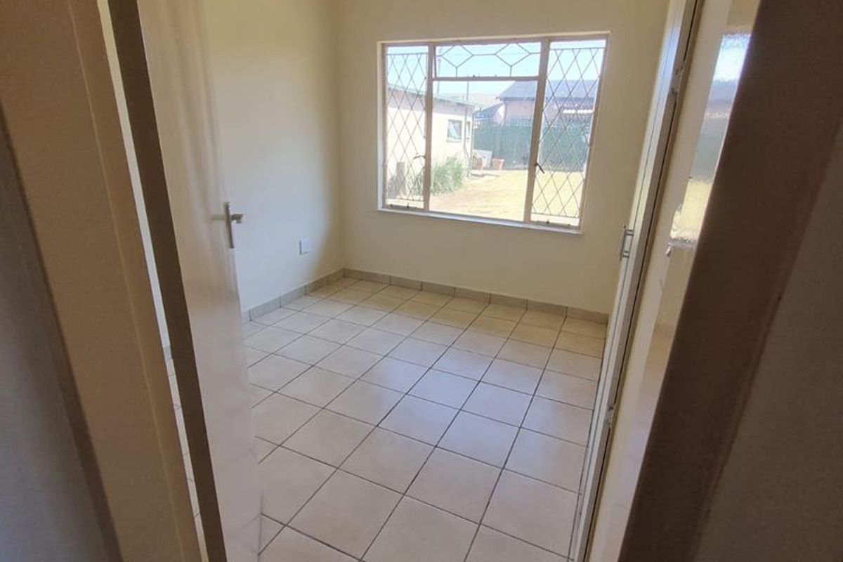 A vacant bedroom featuring neutral tiled flooring, a steel-framed window, and built-in cupboard storage.