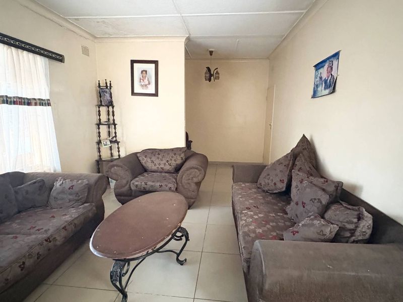 A living room featuring tiled flooring and standard ceiling tiles, requiring cosmetic updates to improve the overall aesthetic and condition of the space.