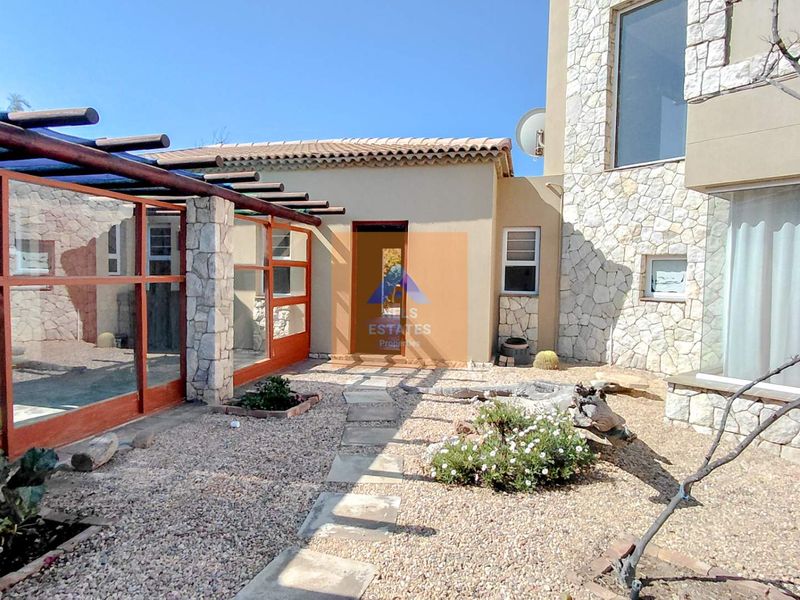 Rear exterior view of the townhouse featuring stone cladding, a gravel garden, a stone pathway, and a covered patio area with a timber pergola.