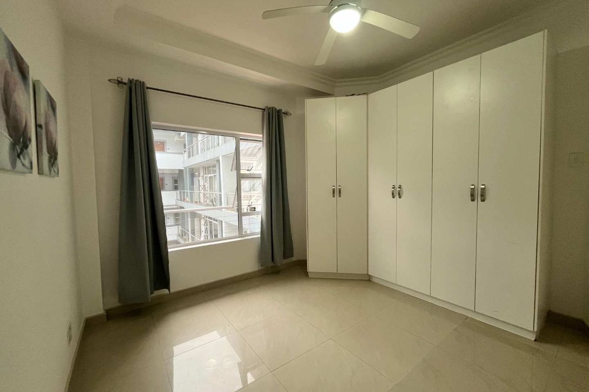 A bright bedroom featuring large white built-in corner wardrobes, tiled flooring, and a ceiling fan, offering a clean and functional living space.