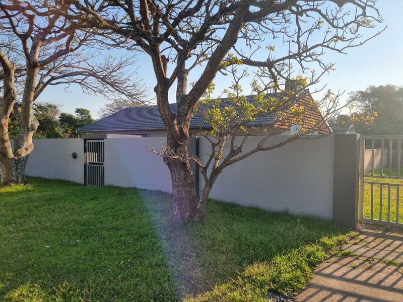 Front view of the property featuring a secure boundary wall, metal gates, and a well-maintained lawn with mature trees.
