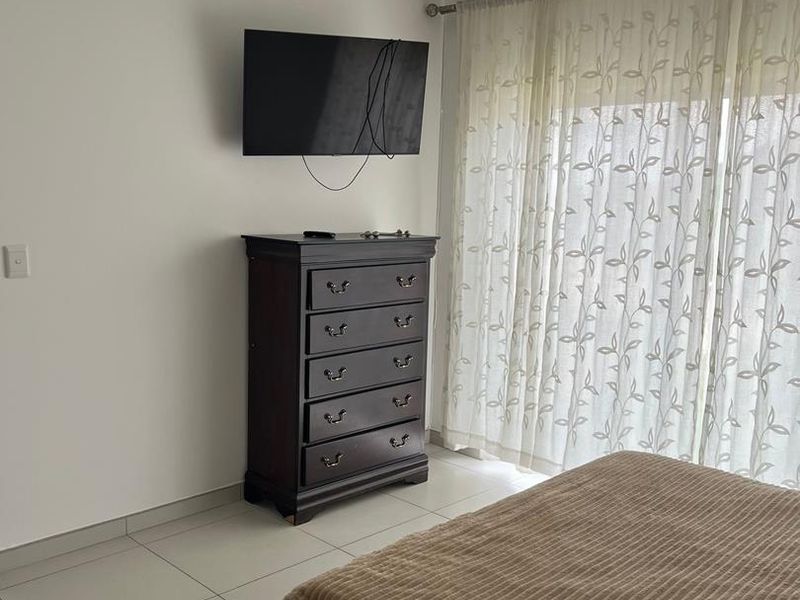 A well-lit bedroom featuring neutral tiled flooring and large windows with sheer curtains, providing a clean and functional living space.