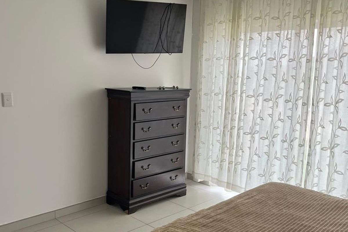 A well-lit bedroom featuring neutral tiled flooring and large windows with sheer curtains, providing a clean and functional living space.