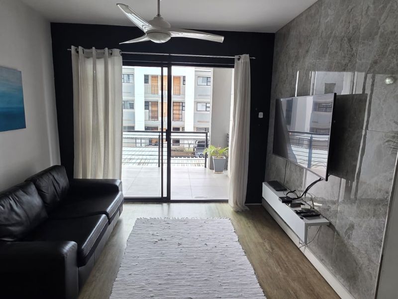 A modern living room featuring marble-effect wall cladding, laminate flooring, a ceiling fan, and direct access to a private balcony through sliding glass doors.