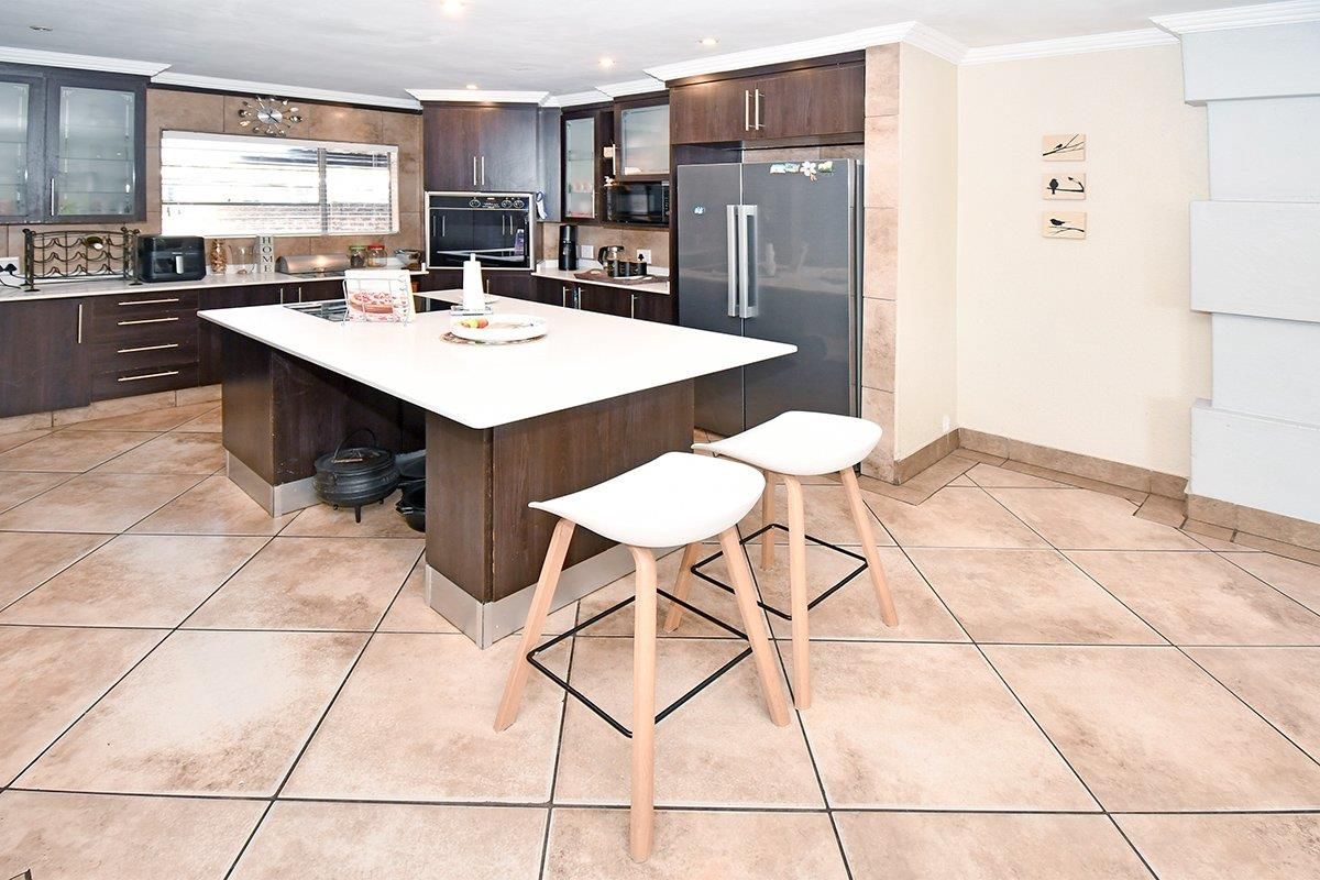 Spacious kitchen featuring a large central island, dark cabinetry, built-in appliances, and neutral tiled flooring throughout.