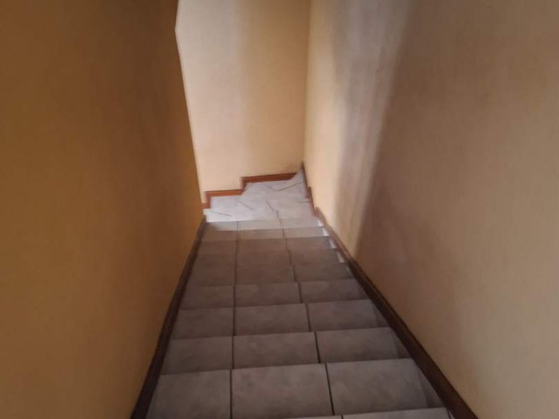 A narrow interior staircase featuring tiled steps and plain painted walls, showing signs of wear and poor lighting.