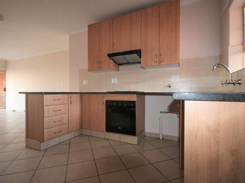 A functional kitchen featuring laminate cabinetry, built-in oven, extractor fan, tiled splashback, and a stainless steel sink, set within an open-plan layout.