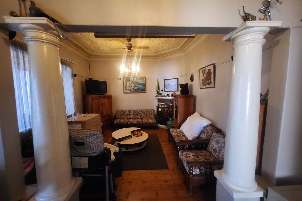 A living room featuring classic decorative columns, an ornate ceiling with a chandelier, and original hardwood flooring.