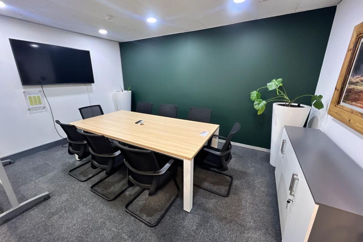 A modern, well-maintained office meeting room featuring a dark green accent wall, recessed ceiling lighting, and professional carpet flooring.
