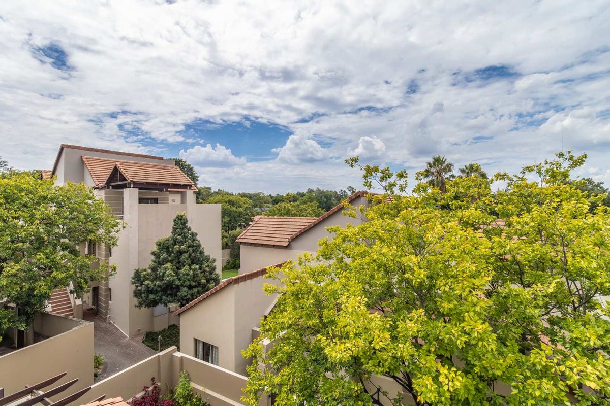 An elevated view of the apartment complex exterior, showcasing the tiled roof architecture, paved pathways, and surrounding mature trees.