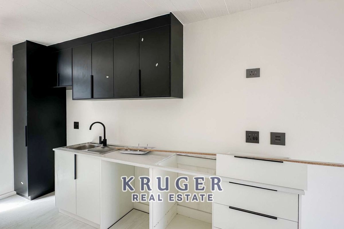 Modern kitchen area featuring matte black upper cabinetry, white lower cabinets, a stainless steel sink with a black faucet, and multiple electrical outlets.
