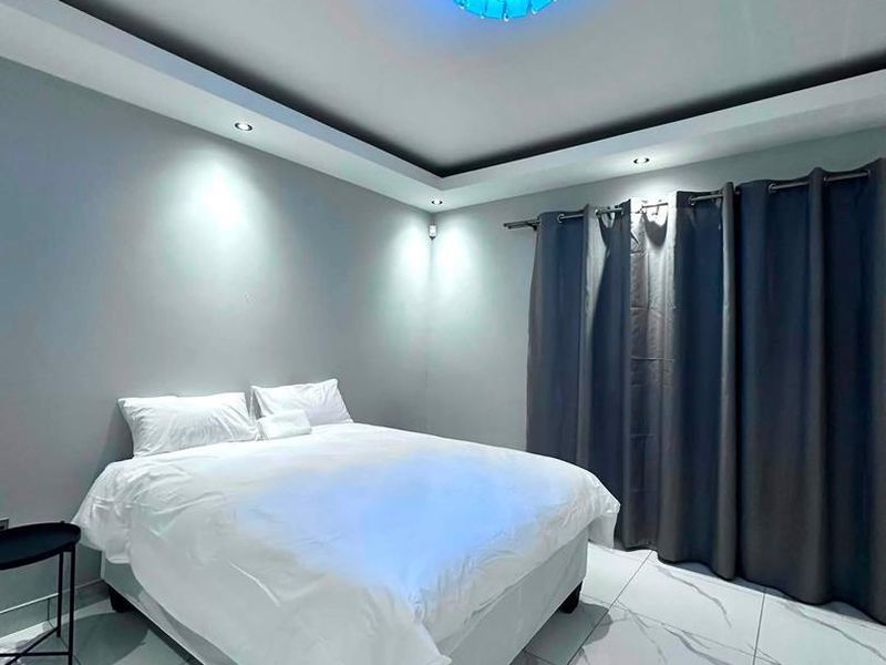 A modern bedroom featuring marble-look floor tiles, a recessed ceiling with downlights, and a contemporary central light fixture.