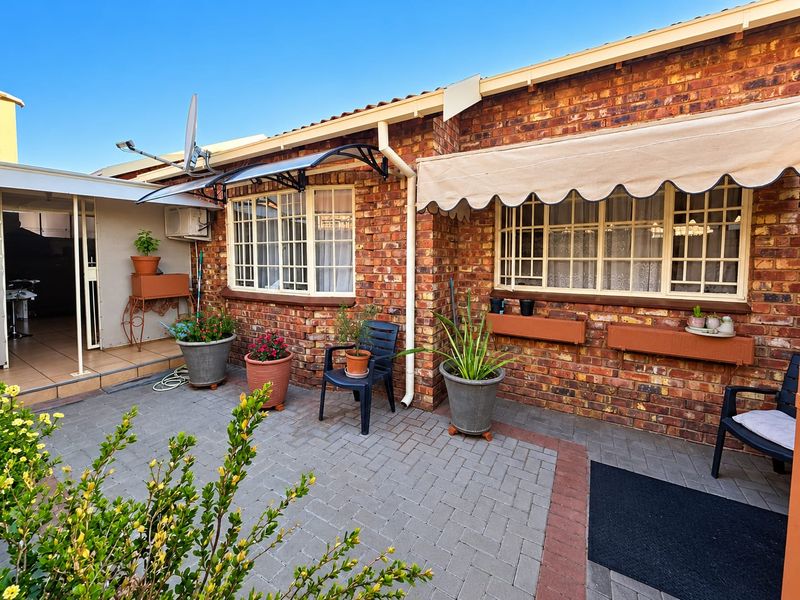 A well-maintained rear townhouse patio featuring face brick exterior, paved flooring, and protective window awnings, providing a functional outdoor living space.