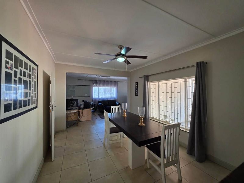 Open plan dining area featuring tiled flooring, ceiling fan, and large windows with security bars, flowing into an adjacent living space.