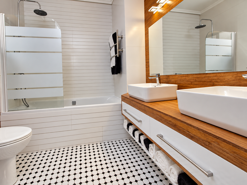 Modern bathroom featuring a double vanity with vessel sinks, a built-in bathtub with a glass screen, and stylish monochrome tiled flooring.