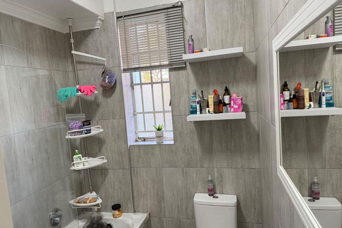 A modern bathroom featuring grey wood-look wall tiles, a built-in bathtub, a dual-flush toilet, and floating storage shelves.