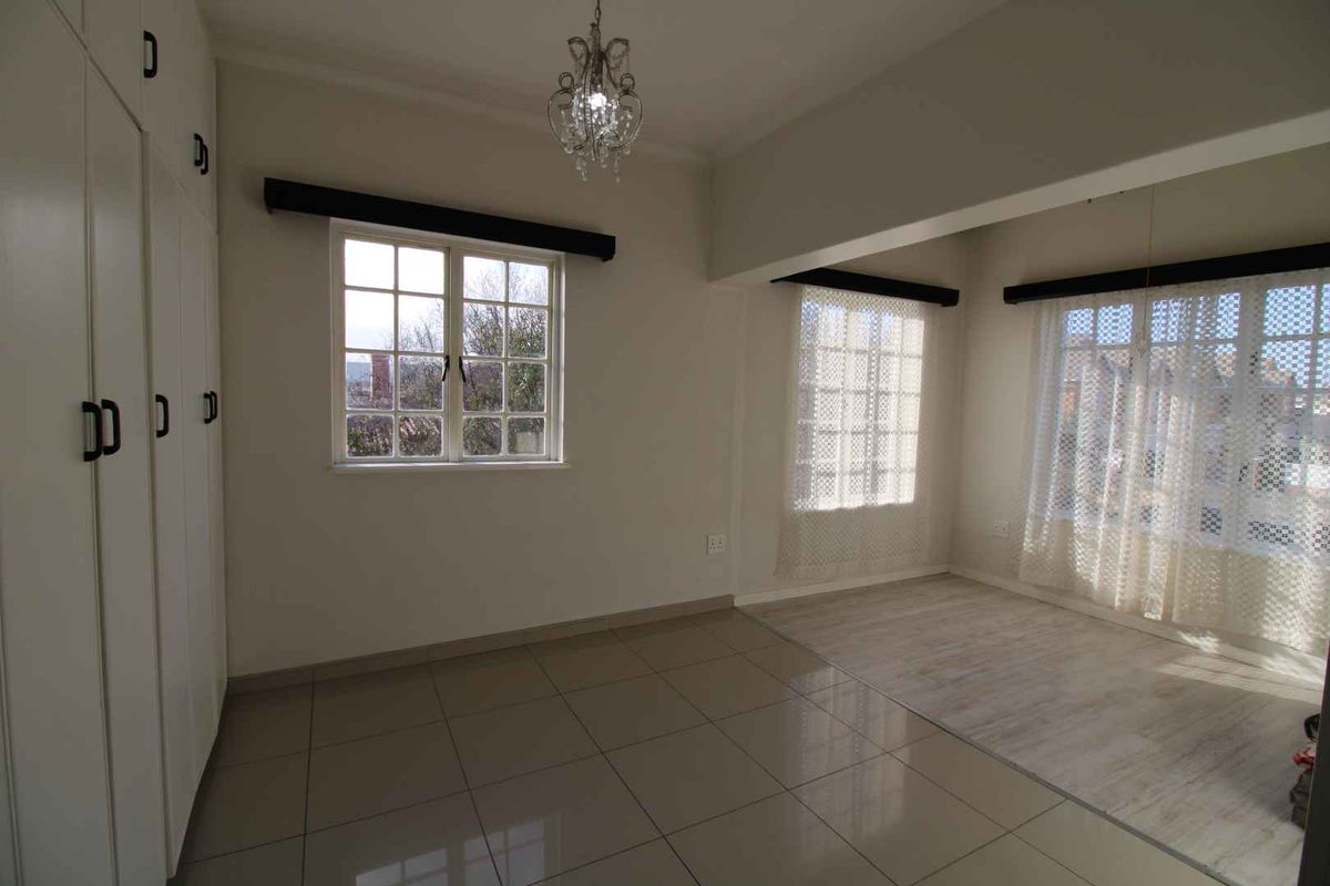 A spacious bedroom featuring built-in cupboards, tiled flooring, and large windows that provide ample natural light.