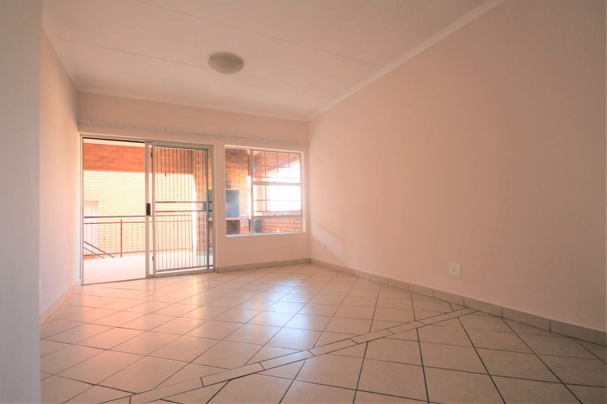 A bright, empty living room featuring tiled flooring, large windows, and a sliding glass door leading to an outdoor area.