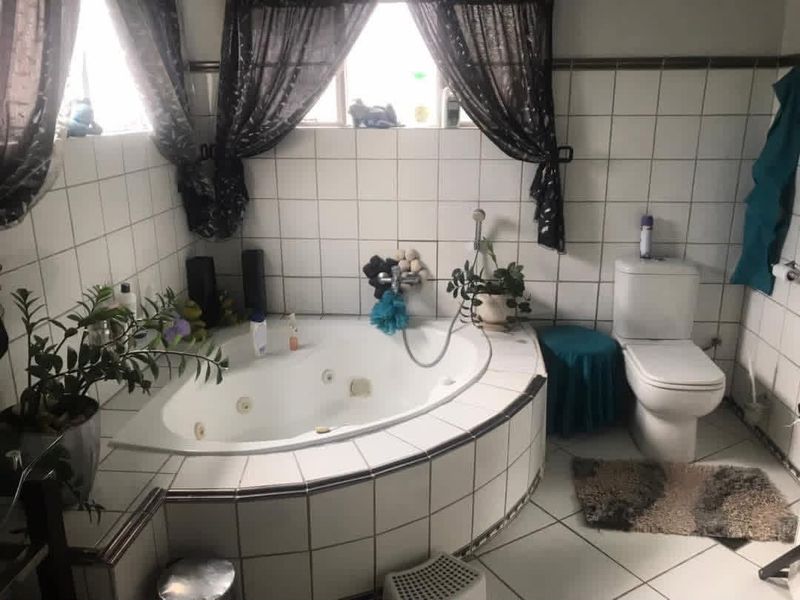 A functional bathroom featuring a corner spa bath, tiled walls and flooring, and a standard toilet.